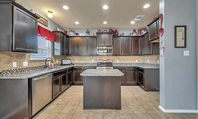 kitchen featuring sink, stainless steel appliances, a kitchen island, and light stone counters