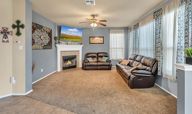 living room with a tiled fireplace, light carpet, and ceiling fan