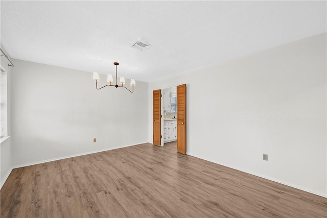 empty room with wood-type flooring and an inviting chandelier