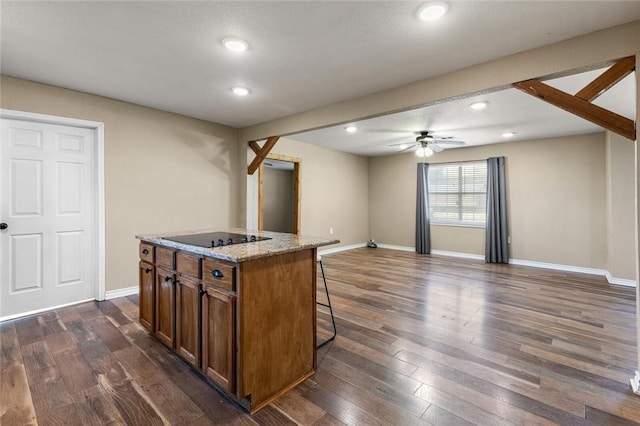 kitchen featuring black electric cooktop, a breakfast bar, an island with sink, and dark hardwood / wood-style floors