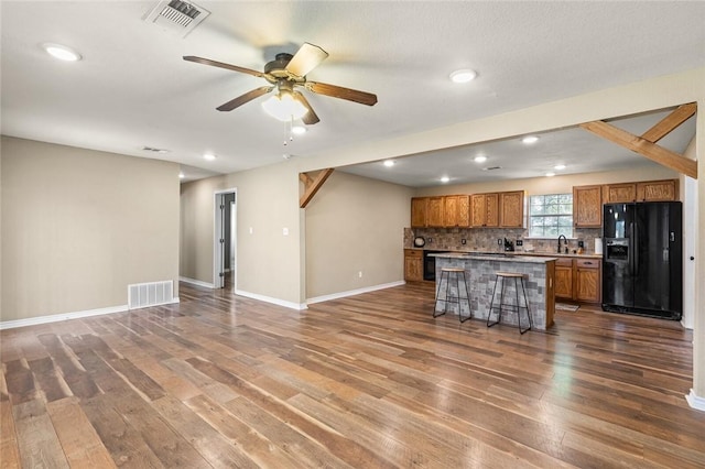 kitchen with a breakfast bar, a center island, hardwood / wood-style flooring, decorative backsplash, and black fridge with ice dispenser