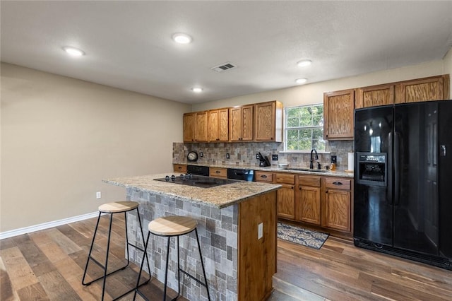 kitchen with light stone counters, a breakfast bar, sink, black appliances, and hardwood / wood-style flooring