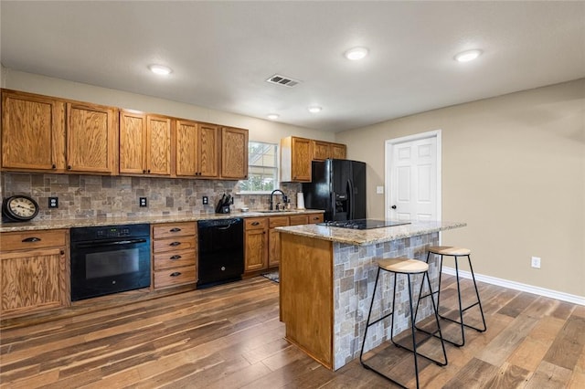 kitchen with black appliances, a center island, a kitchen bar, and dark wood-type flooring