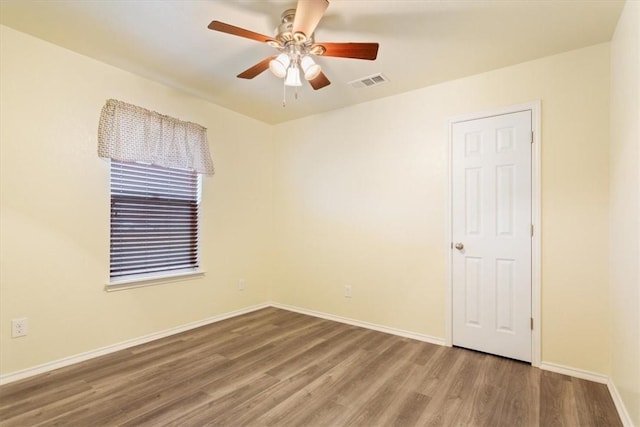 spare room featuring baseboards, visible vents, ceiling fan, and wood finished floors