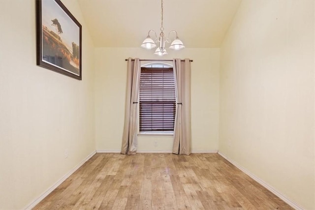 spare room featuring a chandelier, light wood-type flooring, lofted ceiling, and baseboards