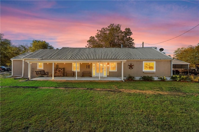 back house at dusk featuring a lawn and a patio