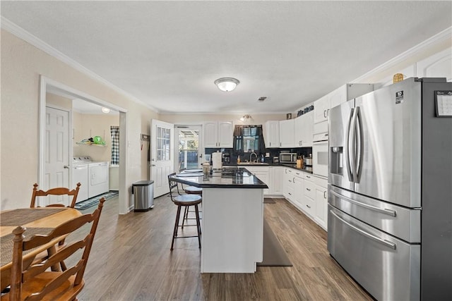 kitchen with a kitchen bar, washing machine and dryer, white cabinetry, and stainless steel appliances