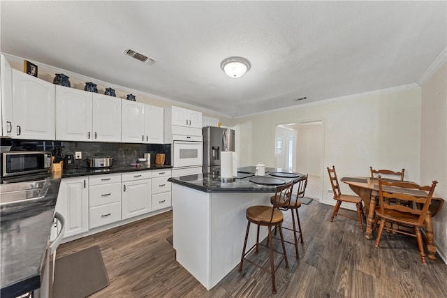 kitchen with appliances with stainless steel finishes, a center island, white cabinetry, and dark wood-type flooring