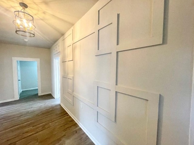 corridor with dark wood-type flooring and a chandelier