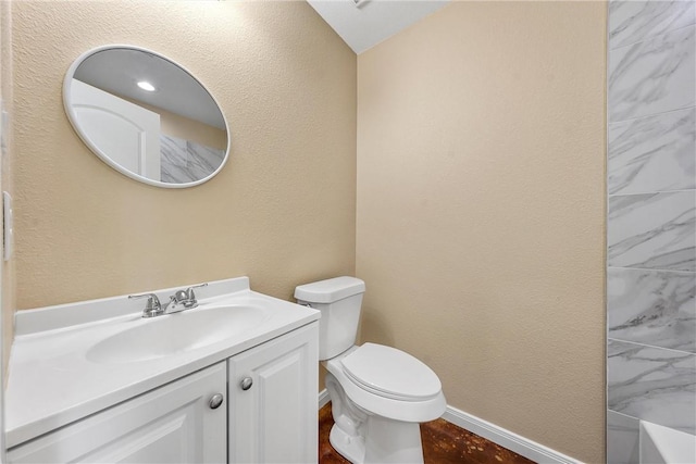 full bath with vanity, baseboards, a tub, toilet, and a textured wall