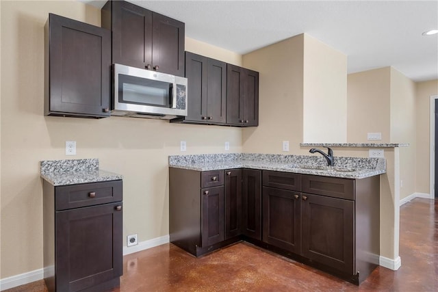 kitchen featuring light stone counters, finished concrete flooring, a peninsula, a sink, and stainless steel microwave