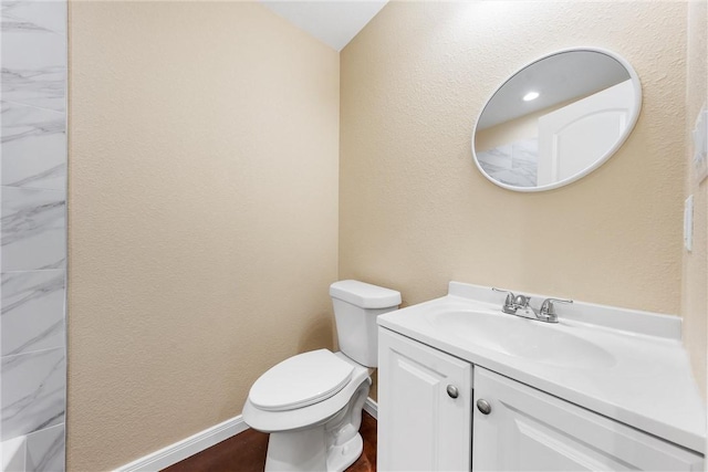 bathroom featuring baseboards, toilet, vanity, and a textured wall