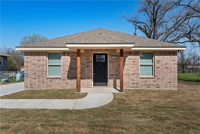 view of front facade with brick siding, a front yard, and a shingled roof