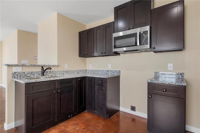 kitchen featuring a sink, stainless steel microwave, baseboards, a peninsula, and light stone countertops