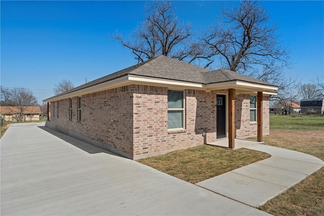 view of front of home with brick siding, a shingled roof, and a front yard