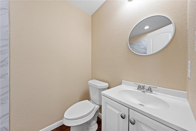 bathroom featuring toilet, vanity, baseboards, and a textured wall