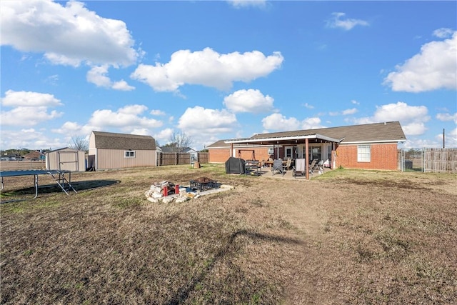 back of house with an outdoor fire pit, a yard, and a storage unit