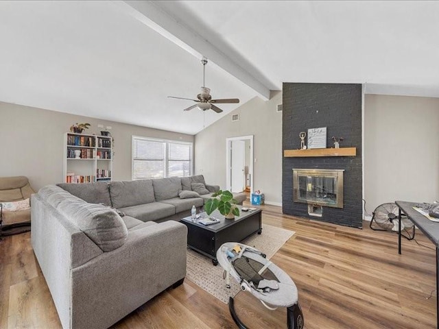 living room featuring hardwood / wood-style floors, lofted ceiling with beams, ceiling fan, and a brick fireplace