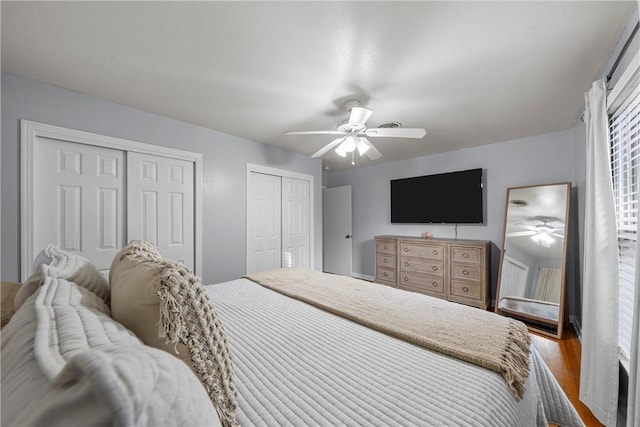 bedroom with hardwood / wood-style flooring, ceiling fan, and multiple closets