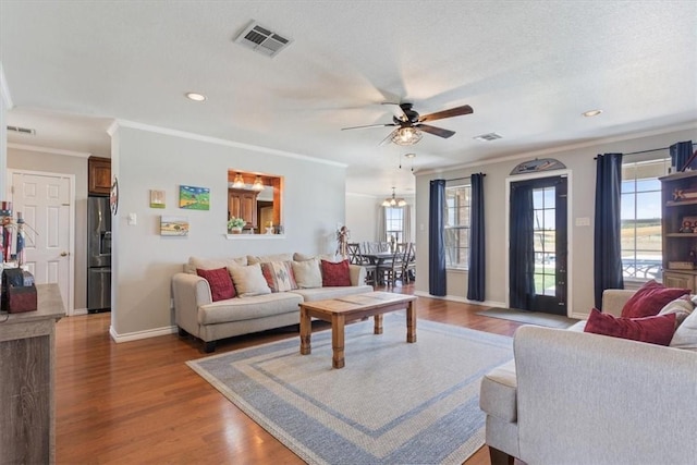 living area featuring visible vents, baseboards, wood finished floors, and ornamental molding