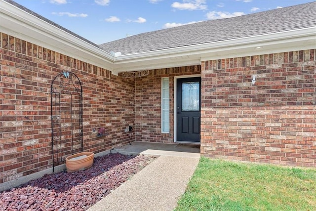 view of exterior entry featuring brick siding and a shingled roof