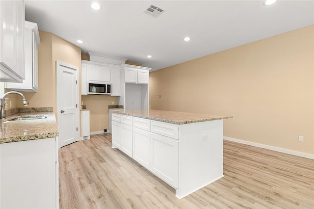 kitchen featuring light stone counters, a kitchen island, sink, light hardwood / wood-style floors, and white cabinetry