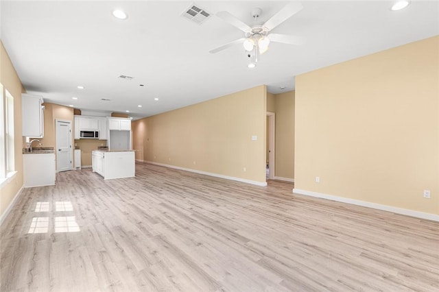 unfurnished living room featuring light hardwood / wood-style floors, ceiling fan, and sink