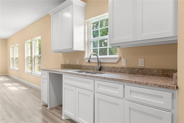 kitchen with white cabinetry, sink, light stone counters, and light hardwood / wood-style flooring