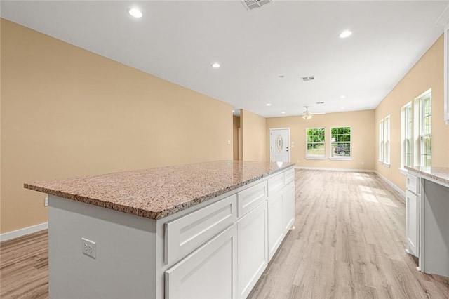 kitchen featuring a center island, white cabinets, ceiling fan, light stone countertops, and light wood-type flooring