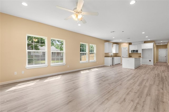 unfurnished living room featuring light wood-type flooring, ceiling fan, and sink