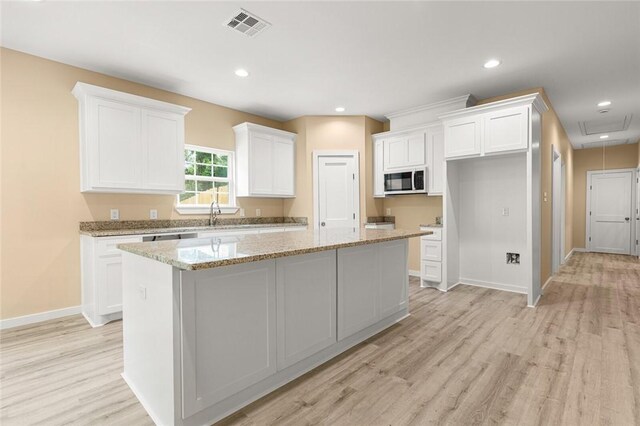 kitchen with light stone counters, a center island, white cabinets, and light wood-type flooring