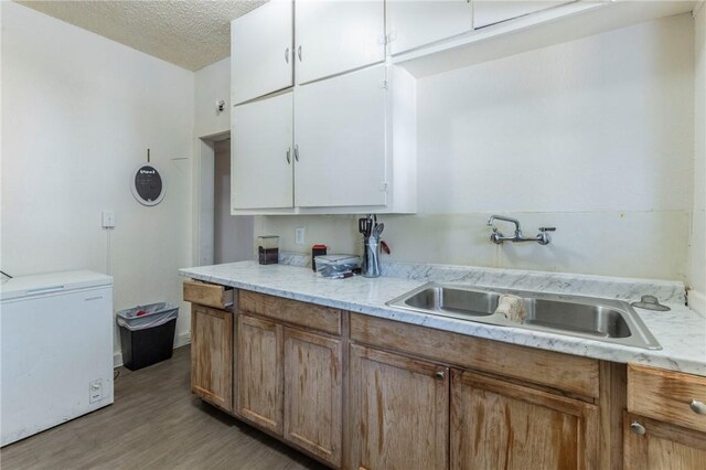 kitchen with sink, a textured ceiling, fridge, white cabinets, and light wood-type flooring