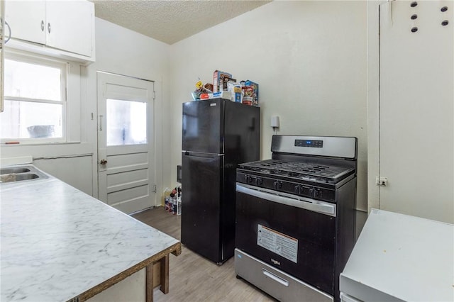 kitchen with white cabinetry, stainless steel range with gas cooktop, light hardwood / wood-style flooring, a textured ceiling, and black refrigerator