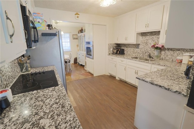 kitchen featuring light stone counters, white cabinets, stainless steel oven, and a sink