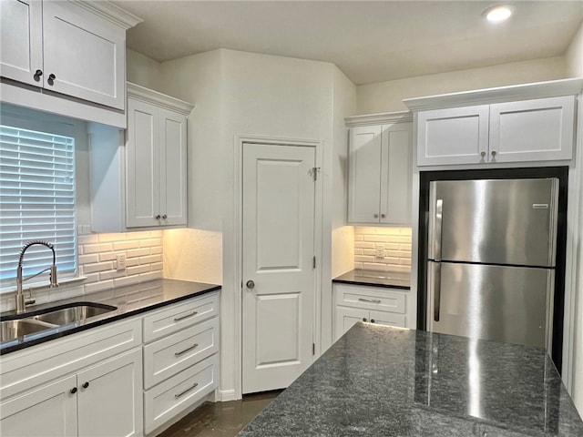 kitchen with dark stone countertops, decorative backsplash, sink, white cabinets, and stainless steel fridge