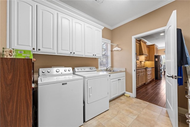 clothes washing area featuring sink, washing machine and clothes dryer, cabinets, a healthy amount of sunlight, and crown molding