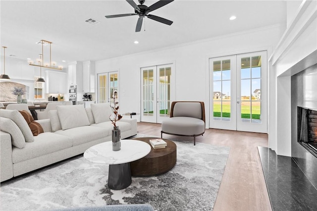 living room featuring a high end fireplace, french doors, ceiling fan, ornamental molding, and wood-type flooring