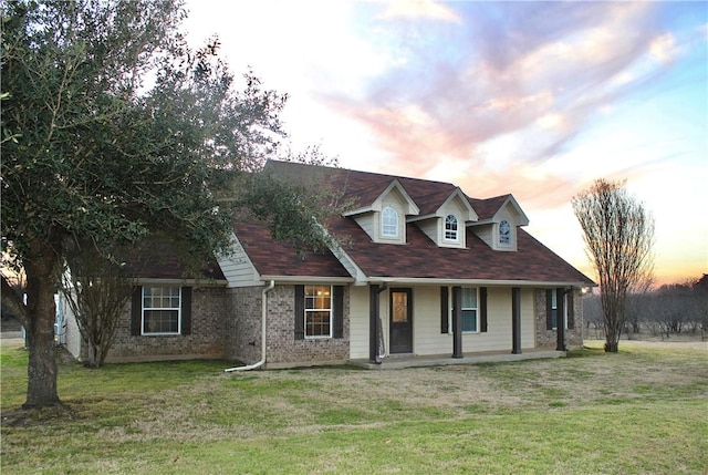 cape cod-style house with covered porch, brick siding, and a front lawn