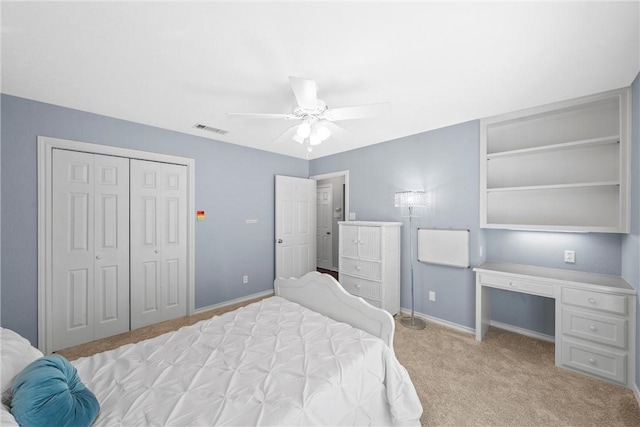 bedroom with built in desk, light carpet, ceiling fan, and a closet