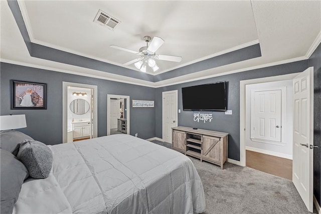 bedroom featuring a tray ceiling, connected bathroom, ceiling fan, and light carpet