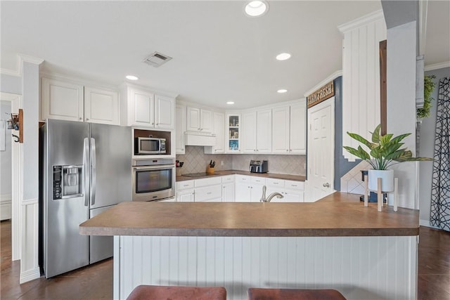 kitchen featuring decorative backsplash, appliances with stainless steel finishes, ornamental molding, white cabinets, and a breakfast bar area