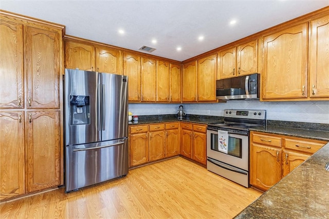 kitchen with stainless steel appliances, dark stone countertops, backsplash, and light hardwood / wood-style floors