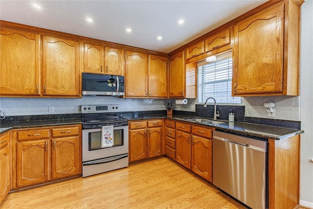 kitchen featuring dark stone countertops, sink, light wood-type flooring, and appliances with stainless steel finishes