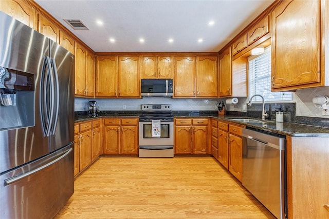 kitchen featuring sink, tasteful backsplash, light hardwood / wood-style flooring, dark stone counters, and stainless steel appliances