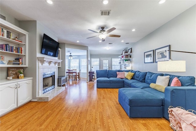 living room with light hardwood / wood-style flooring, a tile fireplace, and ceiling fan