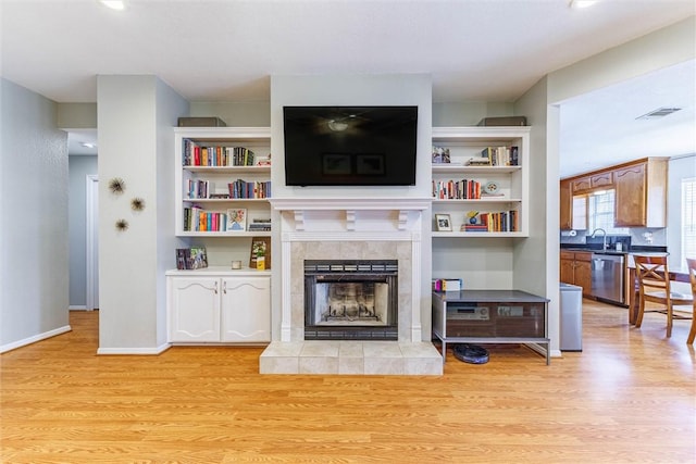 living room with a tile fireplace, sink, and light hardwood / wood-style flooring