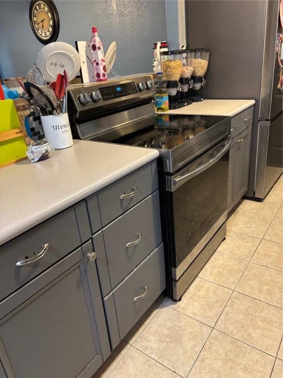 kitchen featuring stainless steel electric range oven, light tile patterned flooring, and gray cabinetry