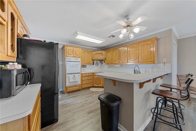 kitchen featuring a breakfast bar, crown molding, light wood-type flooring, kitchen peninsula, and stainless steel appliances