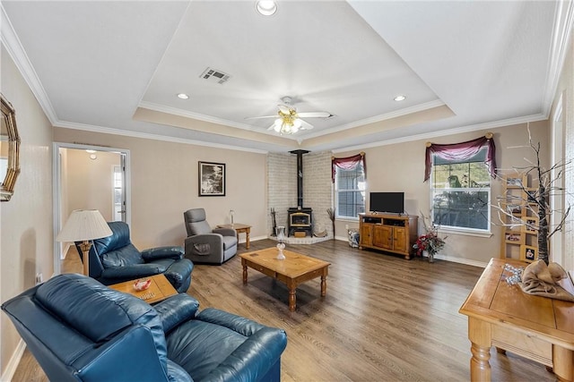 living room with a raised ceiling, a wood stove, crown molding, and hardwood / wood-style floors