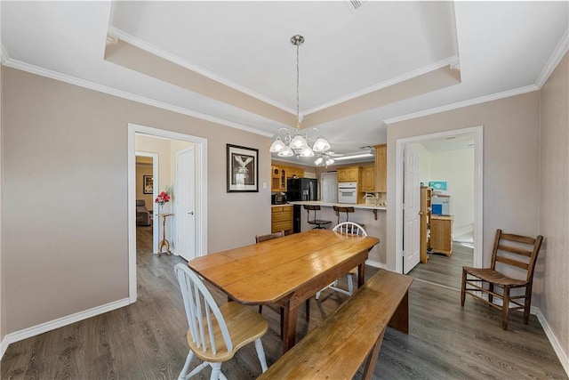 dining space featuring a tray ceiling, a chandelier, wood-type flooring, and ornamental molding